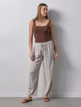 Pantalón de lino a rayas verticales color beige y blanco, con pretina ancha elastizada, lazo de ajuste y bolsillos inclinados.