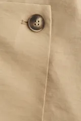 Short pollera color beige, de corte mini y diseño cruzado con botón decorativo.