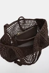 Bolso tipo maxi shopper de rafia tejida en color marrón oscuro, con asas de hombro trenzadas. Incluye un compartimento interior extraíble con cierre de cremallera.