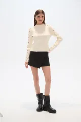 Sweater negro de punto con cuello alto y botones metálicos decorativos en hombros y mangas largas.