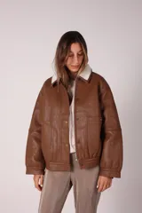 Campera bomber negra de cuero sintético con cuello de corderito blanco, cierre frontal con cremallera y botones a presión, bolsillos laterales y puños y cintura elastizados.