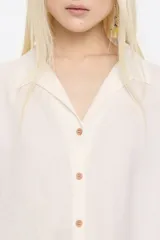 Camisa color crema de corte boxy, confeccionada en mezcla de lino, con cuello camisero, manga 3/4 con sisa ajustable y cierre con botonadura frontal.