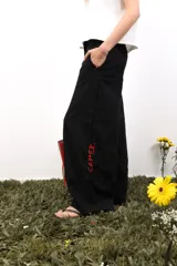 Pantalón blanco de lino, de corte amplio y tiro medio/bajo. Tiene bolsillos delanteros y traseros, botón metálico grabado y bordados laterales y traseros.