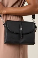 Bandolera negra de ecocuero con correa ajustable y solapa con cierre de botón metálico.
