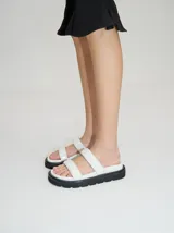 Sandalias blancas con plataforma negra, confeccionadas en cuero vacuno con acabado brillante y doble tira ancha sobre el empeine.