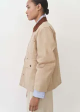 Chaqueta color beige de algodón con cuello marrón de pana, cierre frontal con botones, corte recto, manga larga y cuatro bolsillos frontales.
