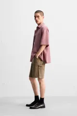 Bermuda color verde militar, de corte relaxed fit, con bolsillos frontales y traseros tipo plaqué, detalle de tira y bolsillo multifunción en la pierna, y bajo irregular.