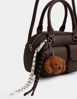 Cartera bowling marrón chocolate de cuerina con doble bolsillo frontal con solapa y broche, cierre superior, correa regulable y desmontable, manijas superiores y charm de perrito.