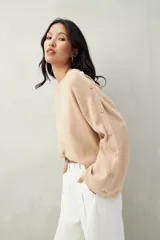 Sweater color beige de tejido de punto, con cuello redondo y mangas largas acampanadas con botones decorativos en los laterales.
