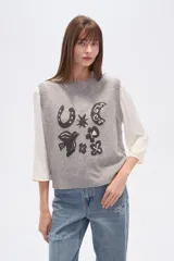 Chaleco de punto sin mangas confeccionado en rayón con efecto confetti en color gris melange. Presenta un diseño frontal en jacquard con diversos motivos como una herradura, una luna, un pájaro y estrellas, con cuello redondo y terminaciones acanaladas.