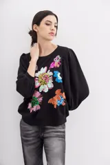Buzo negro de algodón con cuello redondo y mangas largas abullonadas. Presenta apliques de flores bordadas con lentejuelas.