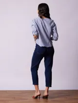Blusa de algodón a rayas verticales azules y blancas, con cuello en V, mangas 3/4 y cierre frontal con botones. Tiene un nudo en la parte delantera.