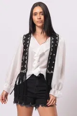 Chaleco negro de gamuza con flecos y bordados blancos en el frente.