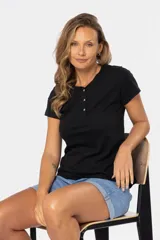 Remera color beige de corte clásico, con cuello redondo y mangas cortas. Presenta una botonadura frontal parcial con botones personalizados.