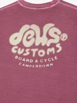 Remera color borgoña con cuello redondo y mangas cortas. Estampado pequeño en el pecho con el logo de la marca Deus Ex Machina.