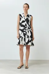 Vestido corto sin mangas, con cuello en V y estampado abstracto en blanco y negro. Tiene cierre frontal con botones y volado en el ruedo.