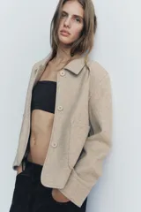 Chaqueta corta negra de cuello solapa y manga larga con puños. Tiene bolsillos de parche en el frente y cierre frontal con botones.