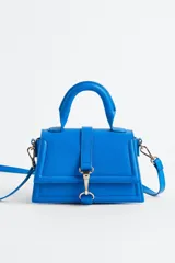 Cartera bandolera azul eléctrico de cuero sintético, con asa corta superior y correa larga extraíble. Tiene solapa con cierre magnético y detalle de hebilla metálica dorada.