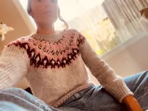 Sweater de punto grueso color gris claro con cuello redondo y diseño con motivos geométricos en tonos rosa y borgoña en la parte superior del pecho y hombros.