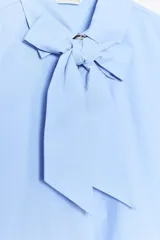 Camisa celeste de cuello redondo y manga larga, con lazo en el delantero y cierre frontal con botones.