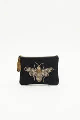 Bolso de mano tipo sobre rectangular de terciopelo negro con cierre dorado y flecos de mostacillas doradas. Presenta un bordado de abeja con canutillos dorados en el frente.