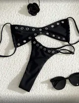 Conjunto de bikini negro con ojalillos metálicos. El corpiño es de corte triangular con tiras finas y la bombacha es tipo tanga.