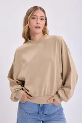 Buzo color beige de corte holgado, con cuello redondo y mangas abullonadas.