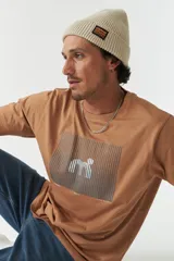 Remera color marrón con estampado rectangular con líneas horizontales y figura geométrica en el centro.