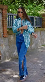 Pantalón de jean azul de tiro medio con spandex y detalle de botones metálicos en la parte inferior de la pierna.