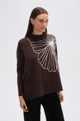 Sweater de tejido marrón oscuro con cuello alto y un gran aplique bordado en blanco con diseño abstracto que simula un abanico o flor.
