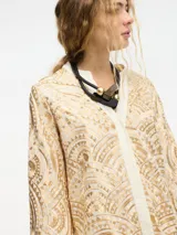 Camisa con estampado geométrico en tonos dorados y negros, con cuello mao y mangas largas acampanadas. Presenta cierre frontal con botones y lazos para atar en la cintura.