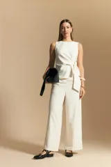 Pantalón de vestir de tiro alto, color beige claro con finas rayas verticales oscuras. Es de corte ancho y largo, con un lazo de tela a juego anudado en la cintura. Se combina con un top sin mangas del mismo tejido y color.