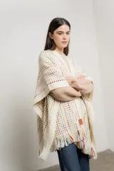 Ruana de tejido crochet color crudo con detalles de hilos de colores y flecos en el borde inferior.