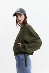 Campera corta color verde militar, sin cuello, con cierre frontal y elástico en la cintura. Tiene bolsillos amplios y mangas largas con puños elásticos.