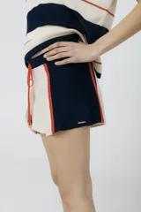 Short tejido en jersey color crudo con cintura elastizada azul marino y cordón rojo. Presenta rayas verticales rojas y laterales en azul marino.
