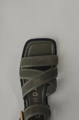 Sandalia plana de cuero color verde militar, con tiras cruzadas en el empeine y una tira ajustable con hebilla metálica dorada en el tobillo.