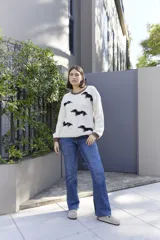 Sweater tejido color crema con cuello y puños acanalados en color naranja. Presenta un diseño bordado de un perro salchicha negro con un moño naranja.