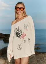 Sweater tejido color crema con cuello amplio que deja un hombro al descubierto. Presenta un estampado con dibujos de estilo boceto en negro y rojo, y detalles de roturas en las mangas.