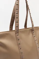 Bolso shopper de símil cuero color beige, con asas largas decoradas con tachas metálicas.