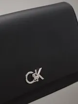 Cartera de hombro negra de cuero sintético con correa ajustable y cierre giratorio. Incluye bolsillo exterior trasero y compartimentos interiores con cremallera.