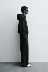 Sudadera negra con capucha, corte boxy, cierre frontal con cremallera, bolsillos laterales y puños elásticos.