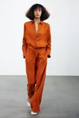 Pantalón palazzo color ladrillo confeccionado en lino 100%, de tiro medio con cintura ajustable con cordones, bolsillos laterales ocultos en costura y pierna ancha.
