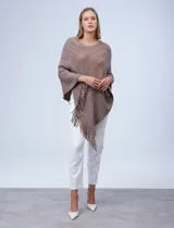 Poncho de tejido suave, color crudo con hilos multicolores que generan un efecto jaspeado en tonos pastel (rosa, celeste, lila). Presenta un diseño asimétrico con cuello redondo y terminación en flecos largos en el ruedo.
