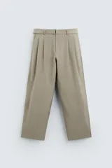 Pantalón color arena de corte amplio, con pliegues frontales, cinturón con hebilla metálica y bolsillos laterales.