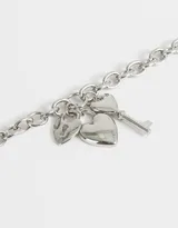 Collar corto dorado con cadena de eslabones gruesos y dijes colgantes: candado con forma de corazón, corazón liso y llave plateados.