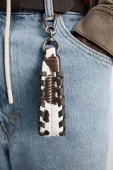Llavero de piel con estampado animal en blanco y marrón, con detalle de costuras laterales y mosquetón metálico plateado.