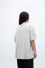 Remera de algodón color beige claro con efecto lavado, corte boxy y manga corta. Estampado frontal con una fotografía en blanco y negro de un local con el texto "LIBERTY LIVES" en rojo. Pequeño texto "CHARM" en la manga izquierda.