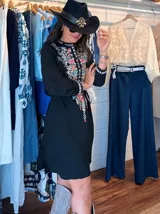 Vestido corto blanco con bordado floral multicolor en el frente, escote redondo con cierre de cremallera parcial y mangas largas.