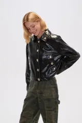 Chaqueta corta marrón de cuero sintético con cuello camisero, cierre frontal con botones metálicos y bolsillos tipo parche con botón.