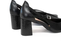Zapato de tacón negro de charol con punta fina, tiras delgadas entrecruzadas sobre el empeine y hebilla plateada lateral. Tacón de bloque texturizado.